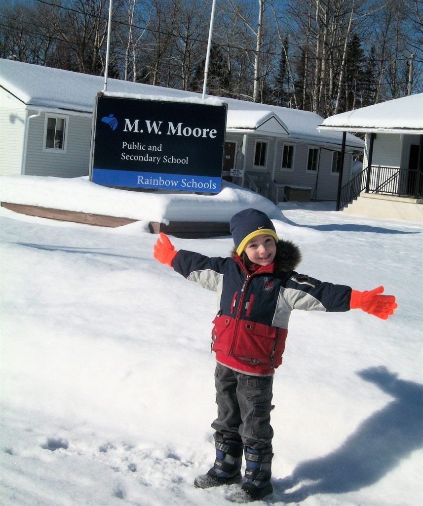 A child stands in front of the M.W. Moore Public and Secondary School