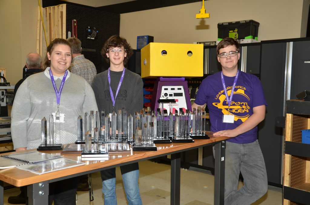 Three students standing with awards won by the FIRST Robotics team